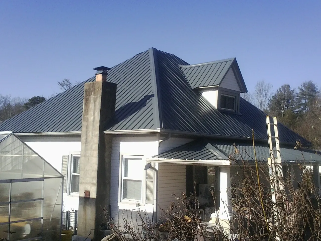 Dark blue standing seam metal roof on a white farmhouse with dormer — Slate & Tile Roof Repair by Roofing Brothers in Hills