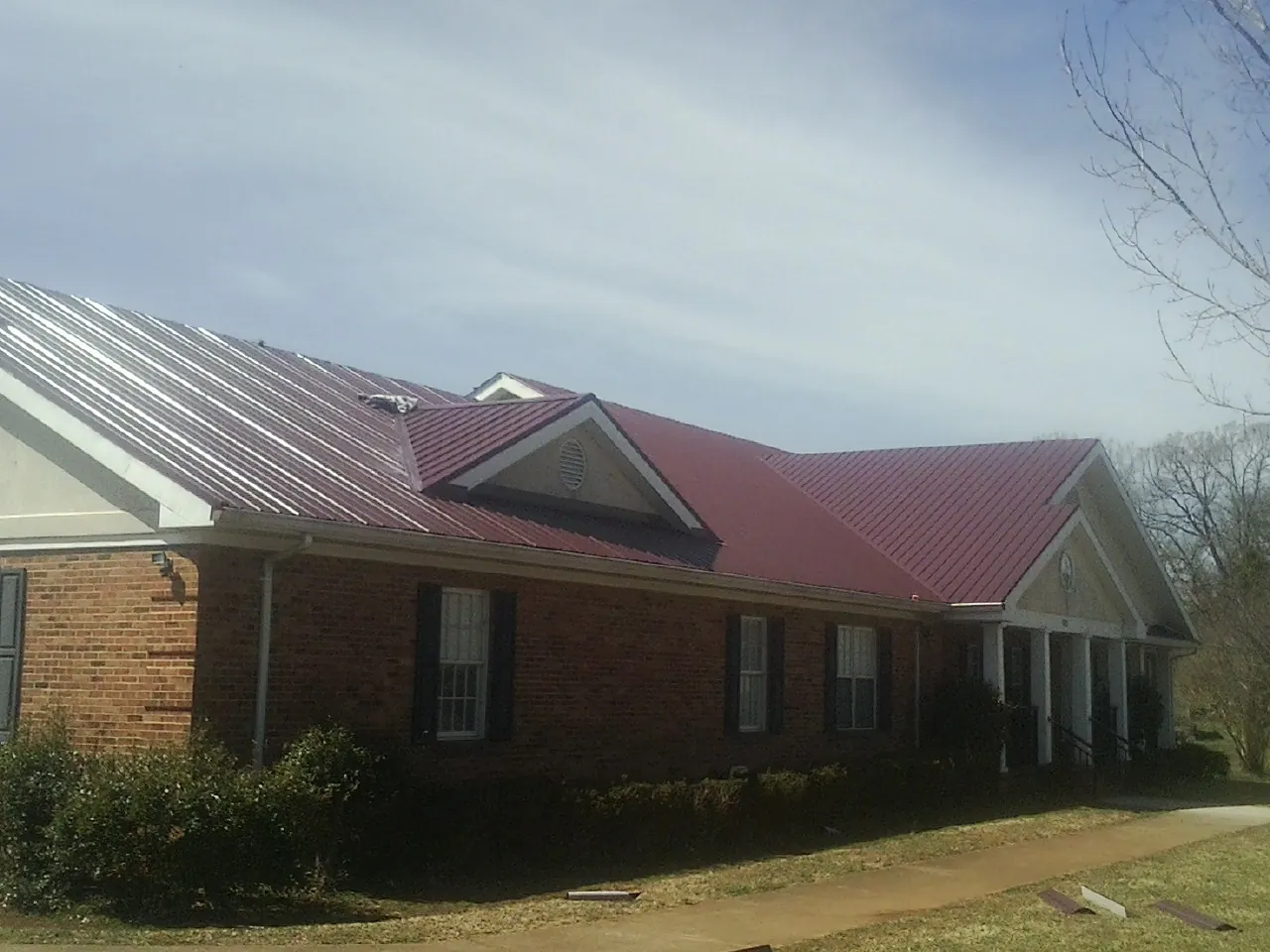 Red metal roof with gabled entries on a long brick building, from a Hail Damage Roof Repair job in Hills