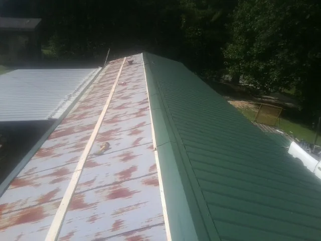Old rusted panels beside newly installed green metal roofing — Wind Damage Roof Repair by Roofing Brothers in Hills