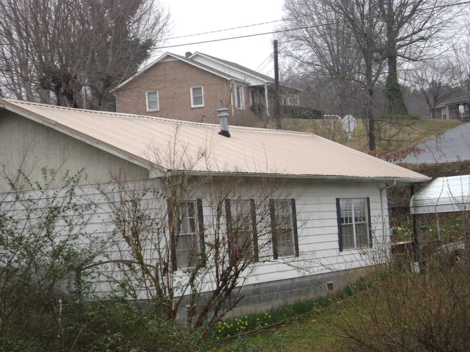 Tan metal roof on a white sided house set into a hillside — Commercial Roofing by Roofing Brothers in Hills