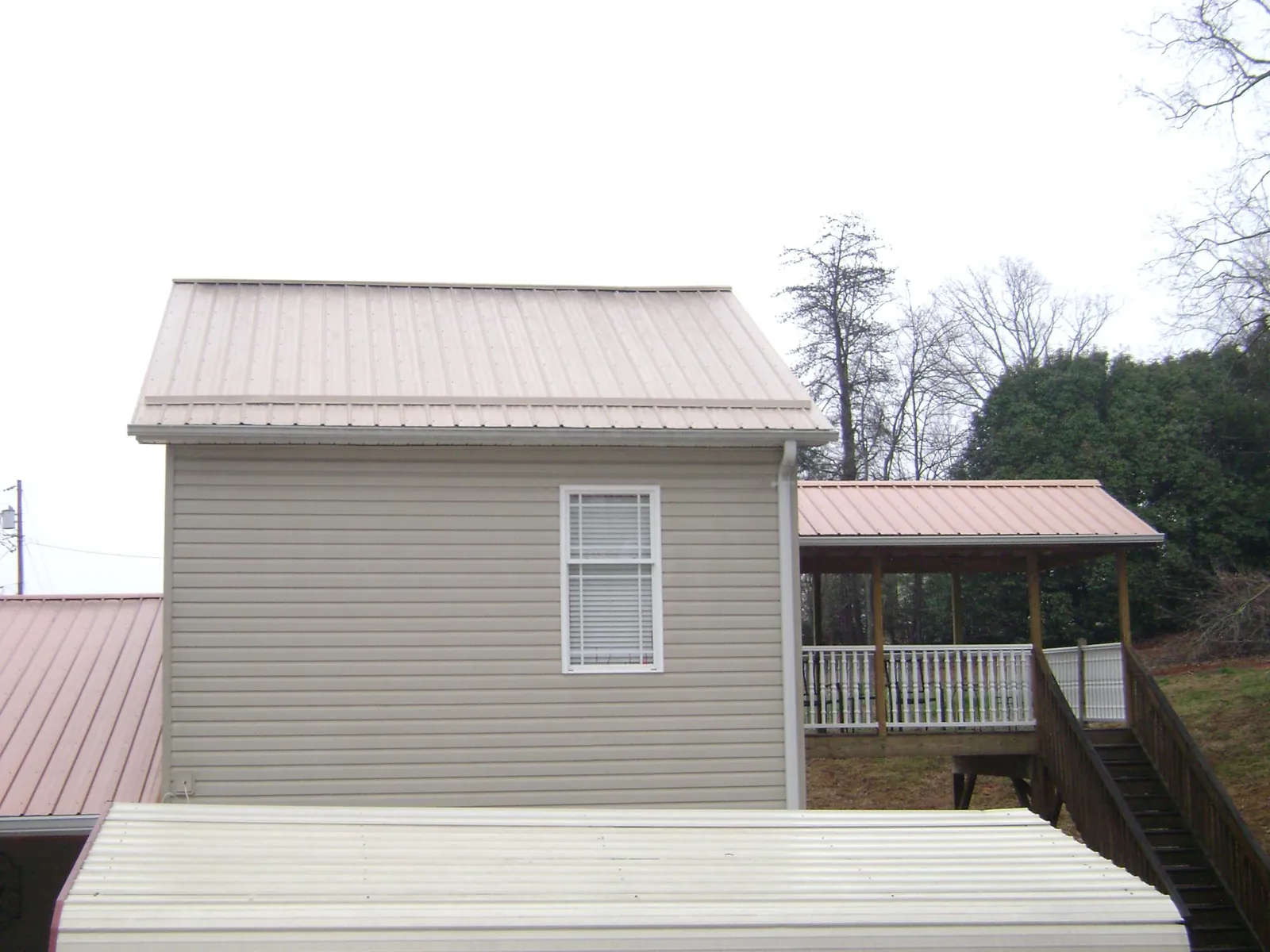 Tan metal roofs on a two story addition and attached porch, from a Roof Replacement job in Hills