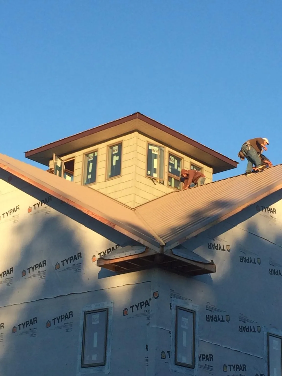 Roofers working around a rooftop cupola on a new metal roof at sunset — Roof Waterproofing in Hills by Roofing Brothers
